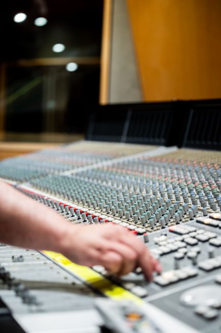 Close-up of a professional hand operating a studio audio mixing console.